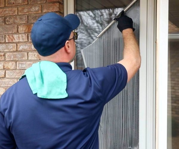 cleaning professional in blue uniform and black gloves cleaning residential window